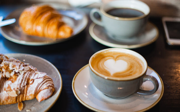 Eine Tasse Café mit Herzschaum und einer ohne. Zwei süße Croissants.